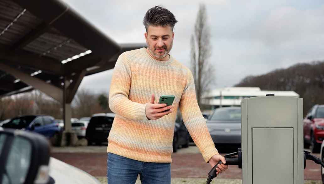 Man met telefoon bij laadpaal