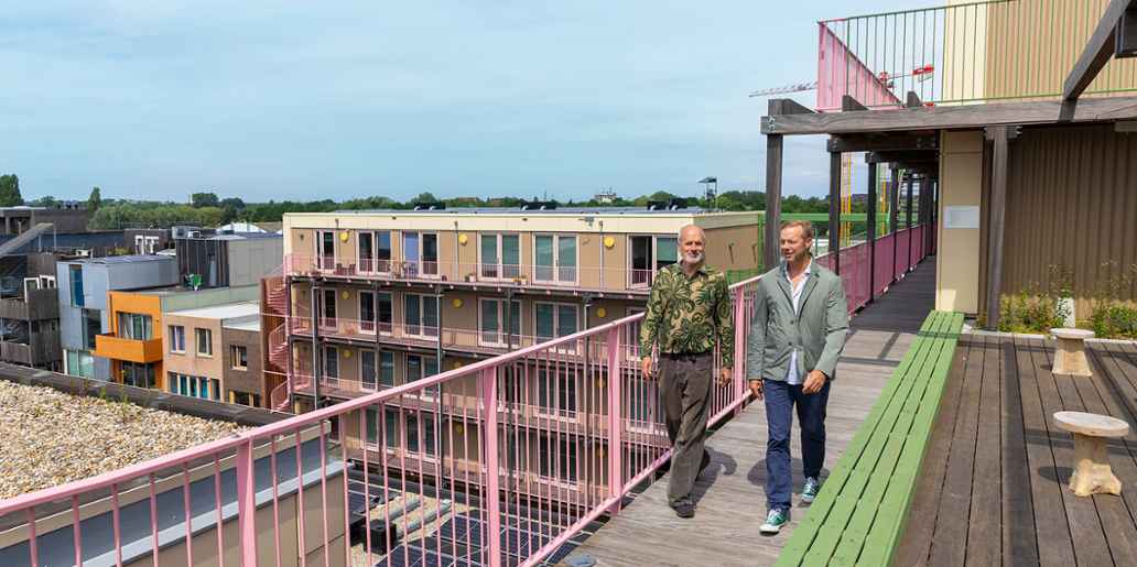 2 mannen lopen over een balkon van het duurzame nieuwbouwproject Mama Poppies