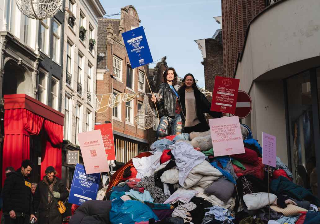 Kiki portesteert op de Kalverstraat, ze staat op een berg van 6.000 kilo kleding.